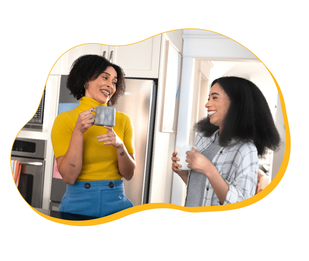 Two women drinking coffee smiling at each other.